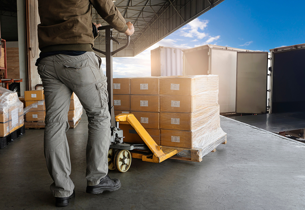 Warehouse Worker Unloading Package Boxes into Cargo Container Truck.Trailer Truck Parked Loading at Dock Warehouse. Delivery Service. Shipping Warehouse Logistics. Freight Truck Transportation.
