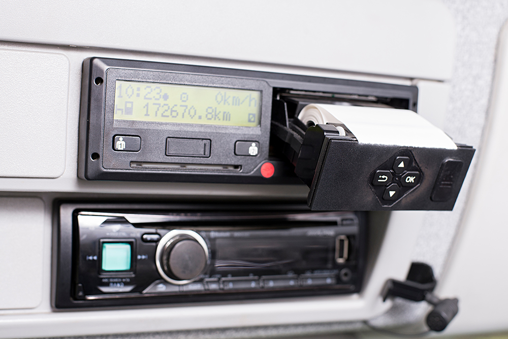 Digital tachograph with open printer and visible roll of paper. Car radio bellow and telephone microphone. Paper Replacement in truck digital tachograph